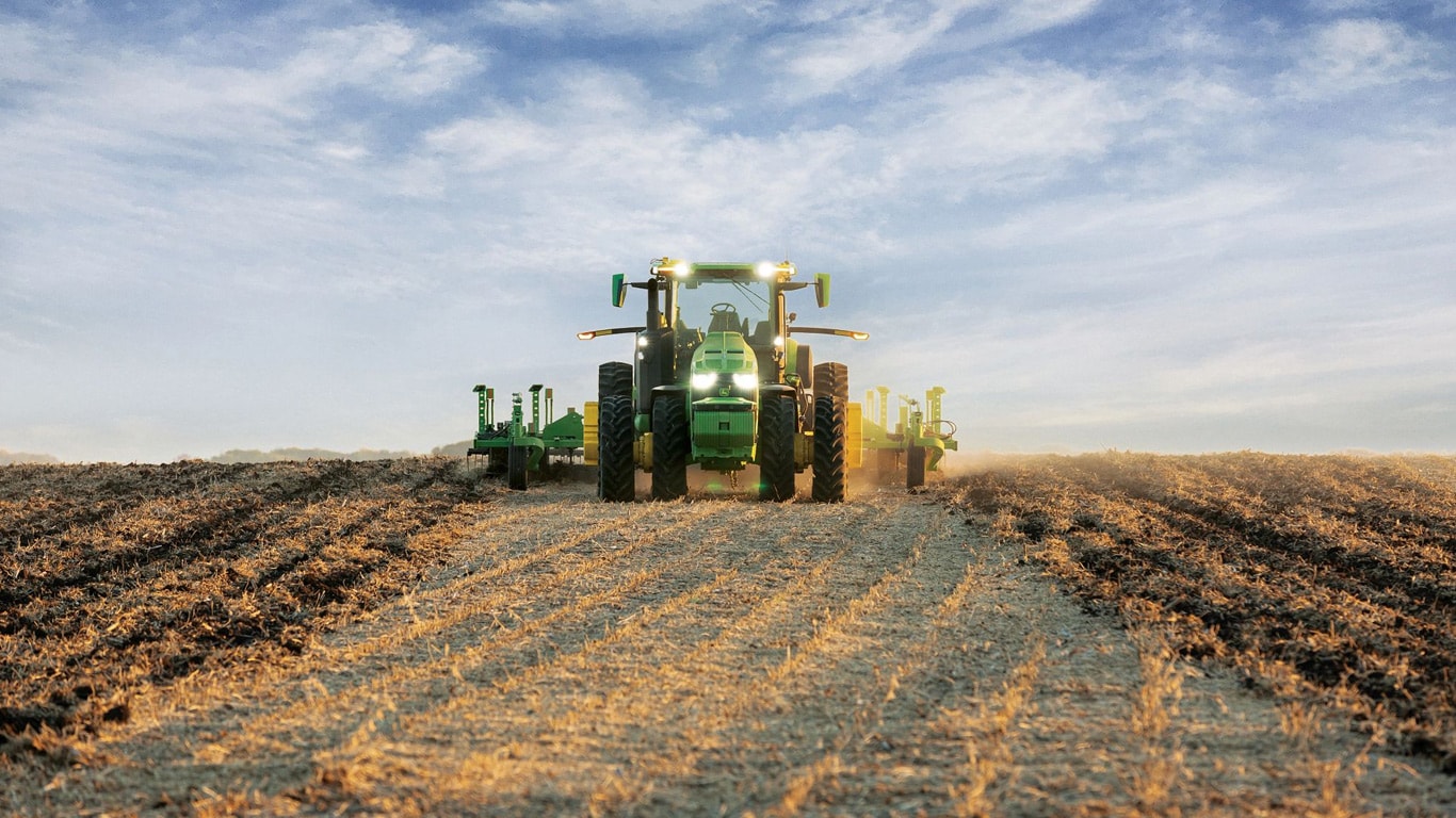 Toprak işleme ekipmanını açık bir tarlada çeken ve kendi kendini sürebilen bir John Deere traktörü.