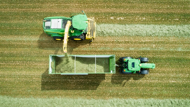 John Deere trakt&ouml;r&uuml;n &ccedil;ektiği vagona y&uuml;kleme yapan John Deere 8000 Serisi ot toplayıcılı kendi y&uuml;r&uuml;r silaj makinesinin hava fotoğrafı