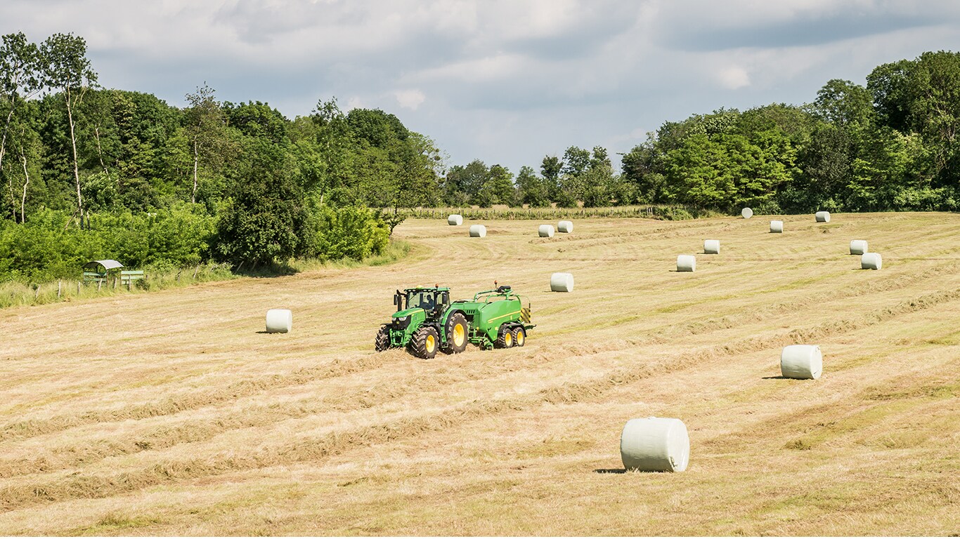 Silaj balyaları bulunan tarlada John Deere traktör ile balya makinesi