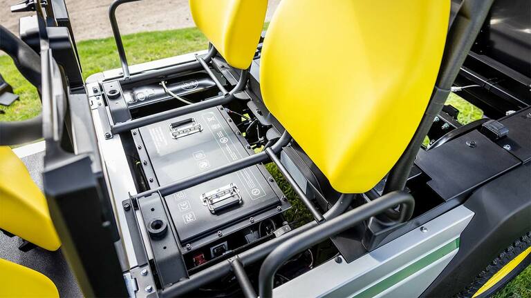 Bir John Deere Gator GS elektrikli hizmet aracında parlak sarı koltukların altına takılmış iki lityum pil takımının yakından görünümü.