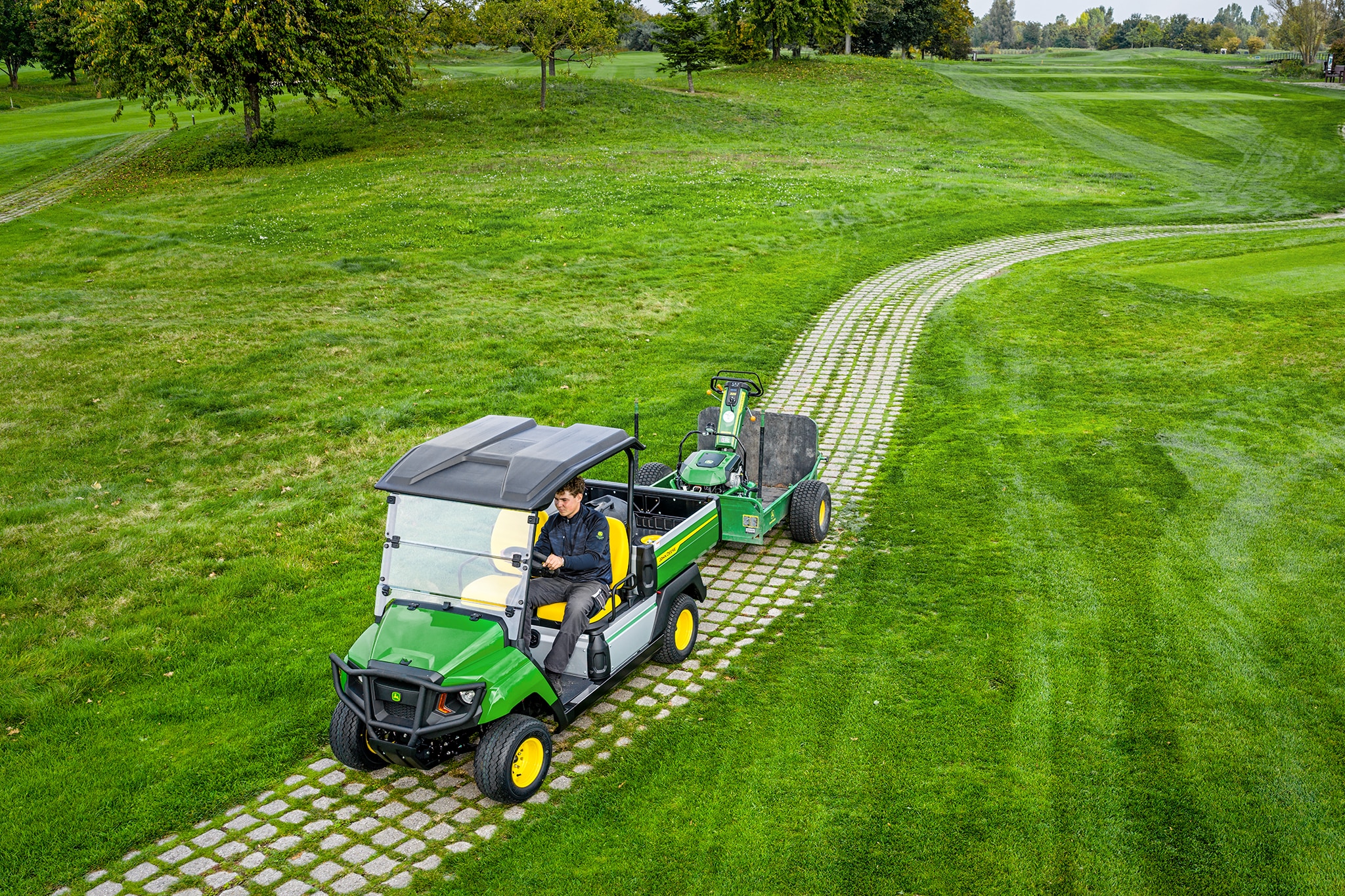 Çim golf sahası yolunda ekipmanı çeken John Deere Gator GS Çim golf sahası yolunda ekipmanı çeken John Deere Gator GS