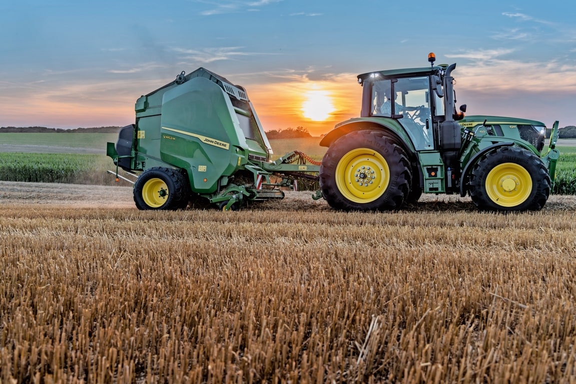 Gün batımında saman tarlasın bir John Deere 6M 150 tarafından çekilen John Deere V462M