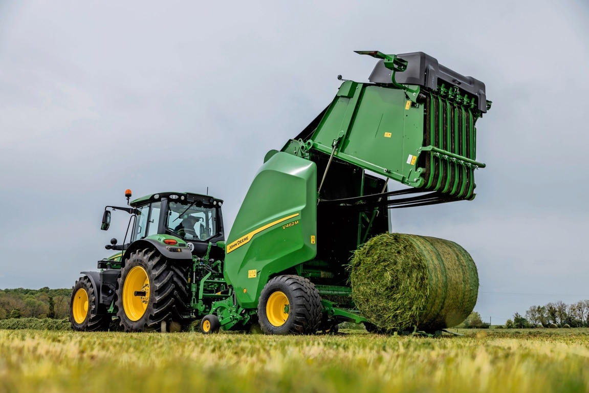 Bir John Deere 6M traktör tarafından çekilen John Deere V462M balya makinesi bir ot balyası çıkarıyor