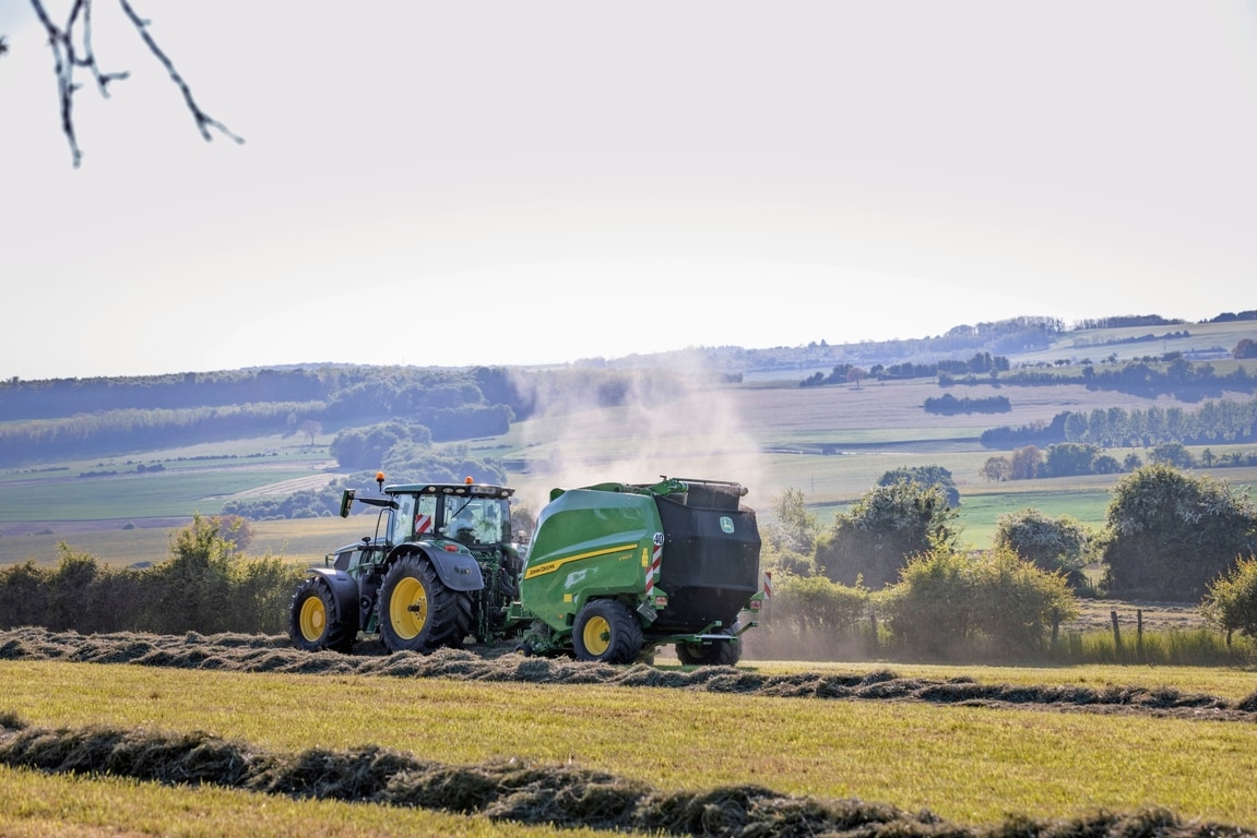 Bir John Deere 6R 185 traktör tarafından çekilen John Deere V462R saman balyalama yapıyor